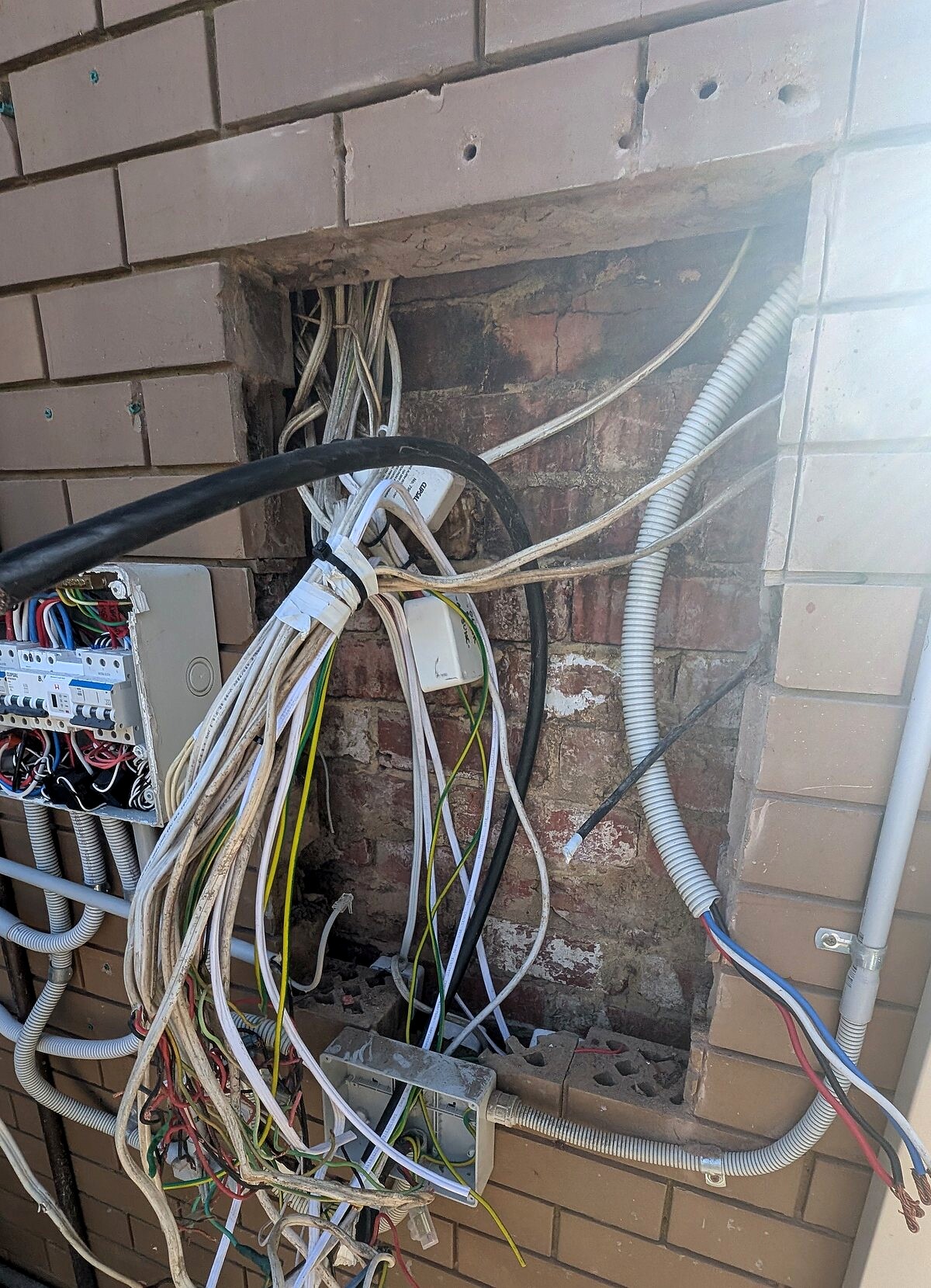 Old switchboard and loose cables on a brick wall before the upgrade